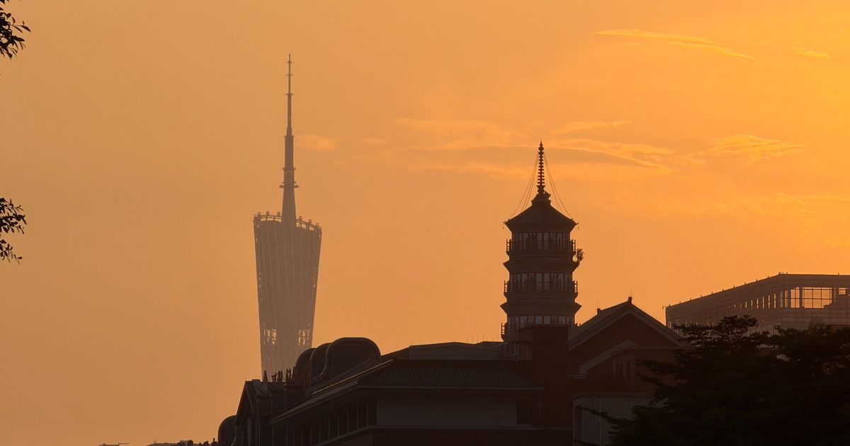 Canton Tower silhouetted against an orange sunset sky above Guangzhou rooftops, with a pagoda-style tower in the foreground, Guangdong Province