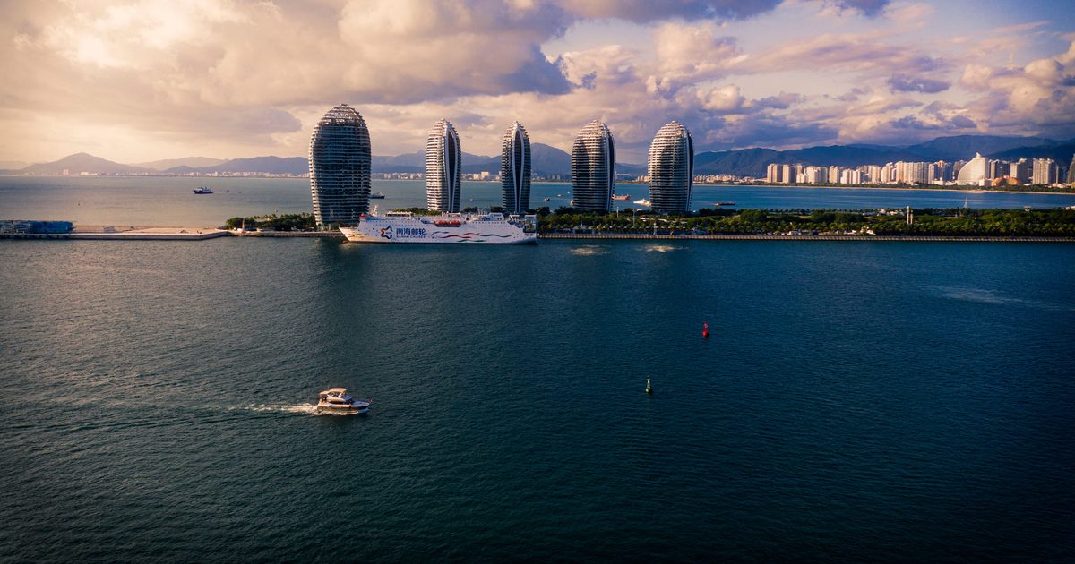 Phoenix Island (凤凰岛) in Sanya, Hainan: five sail-shaped resort towers beside a cruise ship, with the Sanya coastline and mountains behind