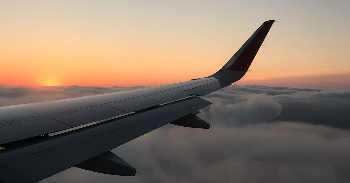 Aeroplane wing and winglet above a layer of clouds at sunset, with the sun on the horizon